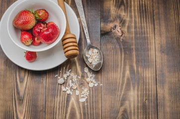 strawberry in a white bowl, honey and a granule in a spoon on a wooden background. Top view, copy...