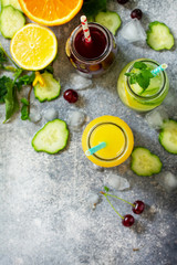 Various refreshments drinks - detox cucumber water, cherry juice and orange juice on stone table. Top view flat lay.