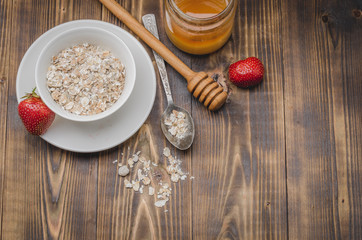 preparation of granule in a white bowl and honey dipper and strawberry on a wooden table. Top view, copyspace