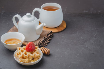 Delicious breakfast with tea, honey and wafers decorated with fresh strawberry on a stone table. Copyspace