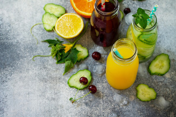 Various refreshments drinks - detox cucumber water, cherry juice and orange juice on stone table. Top view flat lay with copy space for your text.