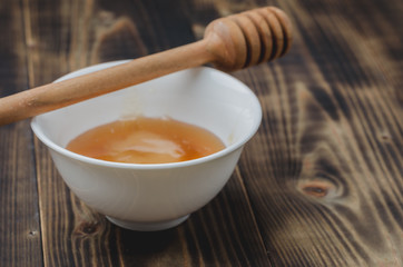 on a wooden background a white bowl with honey and  dipper, selective focus