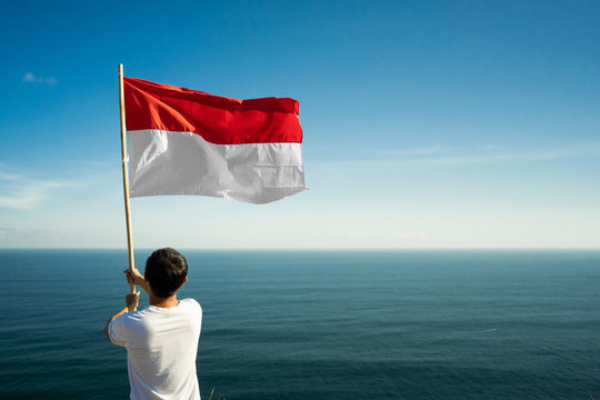 proud indonesian man on a beach cliff raising red and white indonesia flag