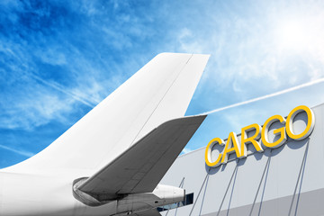 modern airplane tail and freight airport terminal building with cargo lettering isolated on sky background side 3x2 view of passenger jet aircraft with white fin parts of wide body commercial plane