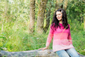 Naklejka na ściany i meble The beautiful brunette in a pink knitted pullover poses outdoors