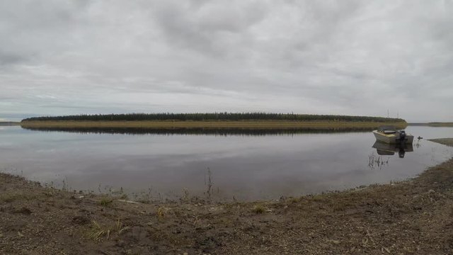 The movement of the taiga river the Vilyui ulus Suntar in Yakutia. Timelapse of water flow and cloudy sky on the shore on the background of mountains and coniferous forest and tied iron Soviet boat.