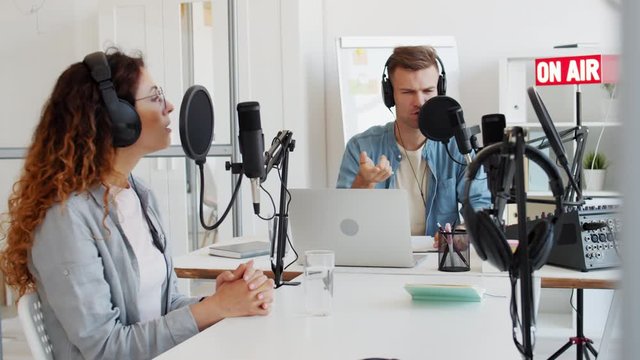 Medium shot of male Caucasian radio host having communication with female redheaded interlocutor sitting nearby in studio