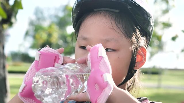 Young Asian girl drinking a bottle of drink while playing roller skating in the park outdoor, lifestyle concept.