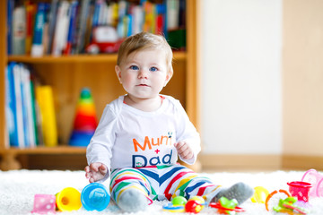 Adorable baby girl playing with educational toys in nursery. Happy healthy child having fun with colorful different toys at home. Baby development and first steps, learning to play and to grab.