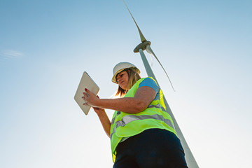 female wind engineer checking a tablet in a turbines field. renewable energy and job technology concept