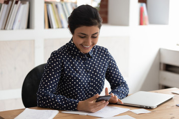 Smiling indian girl distracted from studying using cellphone