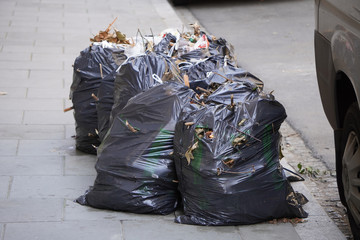 black, knotted bags of household garbage are on the road for loading into the garbage truck. waste...
