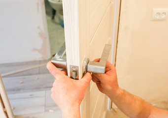 Man is installing the doors handle. Repair works. Maintenance in the apartment.