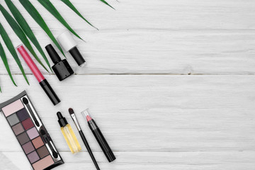 Various makeup cosmetics and a green palm leaf flat lay white wooden table background with a copy space.