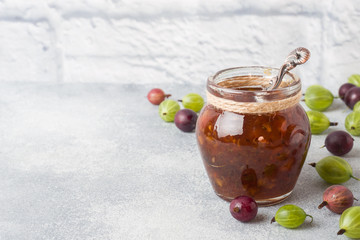 Gooseberry jam in a jar with fresh gooseberry berries on a gray background. Copy space.