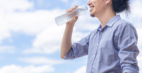 A happy business man drink cold water from plastic bottle during summer in day time and bright beautiful blue sky, hydration and health concept.