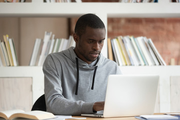 Serious black male student studying with laptop at home