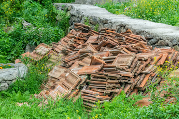 A big pile of old brown roof tiles lay on the grass on a sunny day.