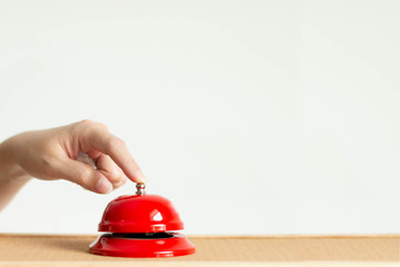 Close-up of index finger pressing the bell button of red vintage style handbell on wooden table.