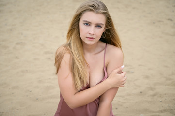 Young woman in pink dress sitting on sand and enjoys sea.