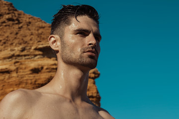 Strong face male model on the nature background with rocks and water on the beach on the sunset