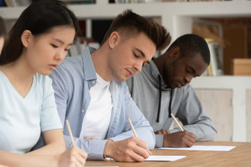 Focused multiethnic young people write passing exam at school