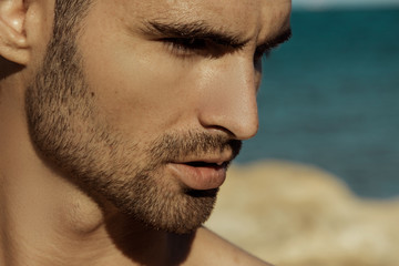 Obraz premium Strong face male model on the nature background with rocks and water on the beach on the sunset