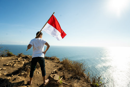 Proud Indonesian Man On A Beach Cliff Raising Red And White Indonesia Flag