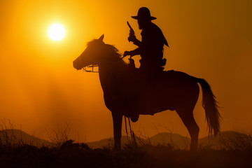 Cowboy riding a horse carrying a gun in sunset with mountain scene in Pakchong, Nakhonratchasima, Thailand