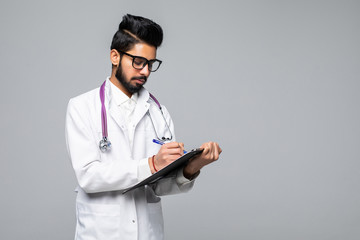 Young indian man doctor with stethoscope over neck holding clipboard isolated on white