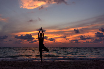 Fototapeta na wymiar Silhouette of girl doing yoga on the beach during sunrise