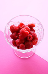 Fresh, red raspberries in a crystal bowl isolated on coloured pink background with a geometric shape