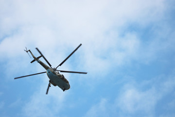 Fototapeta na wymiar Military helicopter in flight on background of blue sky with white clouds. Bottom view, air forces concept
