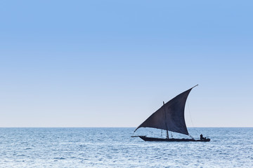 Fototapeta na wymiar Traditional dhow sailing vessel used to transport people goods and commodities silhouetted against a blue coean and sky