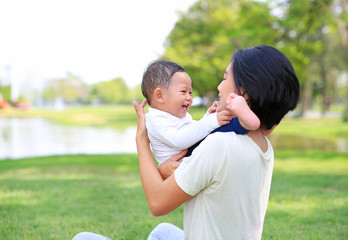 Happy family Asian mom and her son playing in the nature garden. Mother carrying son.