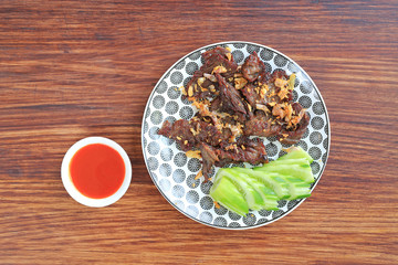 Deep fried beef served with sliced cucumber and sweet chili sauce on wooden board background. Top view.