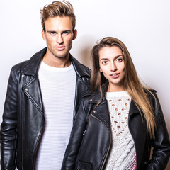 Young beautiful couple in black leather jackets pose in studio.