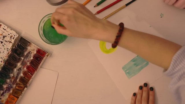 Close up student painting in watercolors using a paintbrush on watercolors paper. Study design tutorial animator illustrator work freelance session art home studio loft