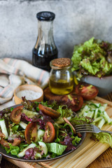 Cucumber salad with tomatoes and herbs on a wooden tray on the background of the sauce, olive oil and a bowl of salad and salt