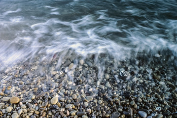 Landscape of stony beach. Wild stone beach with waves. The pebble stones are lying on the sea sand beach. Mystical background