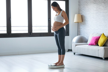 Pretty young pregnant woman standing on scales at home.