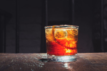 Cracked whisky glass. Alcohol cocktail with beautiful backlight on a wooden table. Served with ice and orange peel. Boulvardier or Negroni.