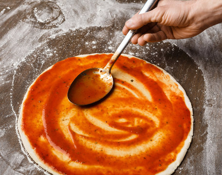 Spreading tomato sause on pizza base, closeup