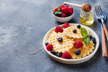 Corrugated waffle cookies with fresh raspberries and blueberries on a dark concrete background. Copy space.