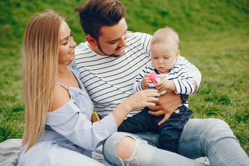 A young and beautiful blonde mother in a blue dress, along with her handsome man dressed in a white jacket, siting with her little son in the summer solar park