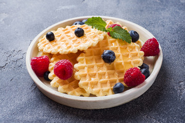 Corrugated waffle cookies with fresh raspberries and blueberries on a dark concrete background. Copy space.