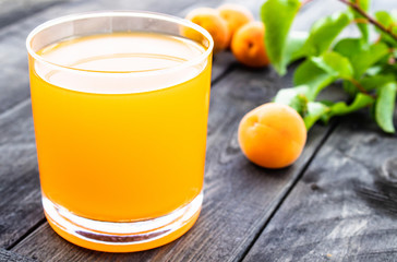 Fresh apricot juice with apricots and a branch with green leaves on the background of old boards.