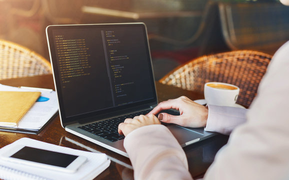 Young woman programmer writing code on laptop in cafe