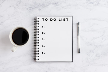 To do list numbered writing on notebook. Notebook on desk with coffee cup and a pen.