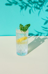 Summer Basil lemon smash cocktail isolated on a turquoise wall with plant shadows in the background